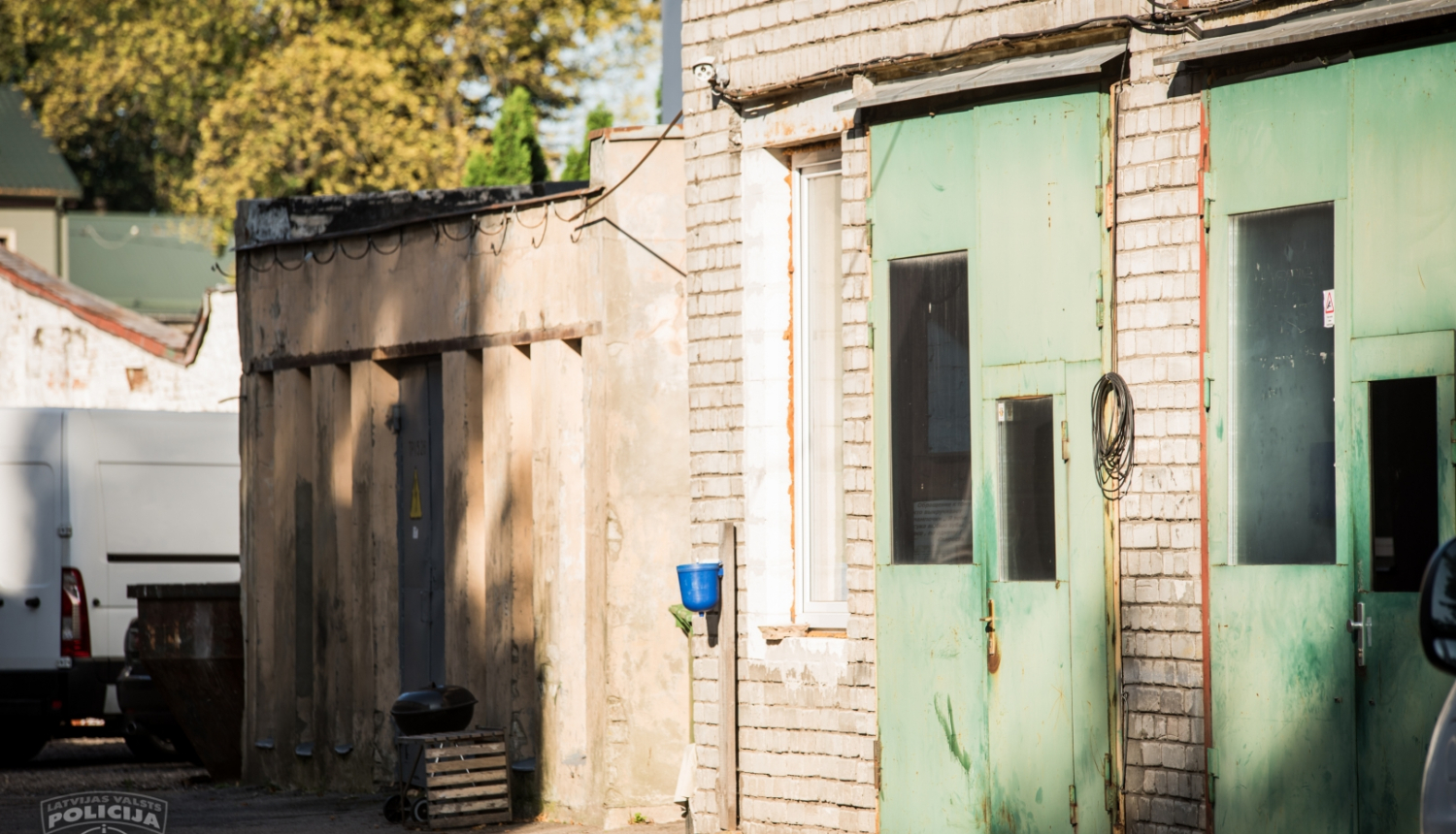 Pagalms, kurā redzamas saimniecības ēkas, viena ēka mazāka, otra ēka ar divām lielām zaļām durvīm