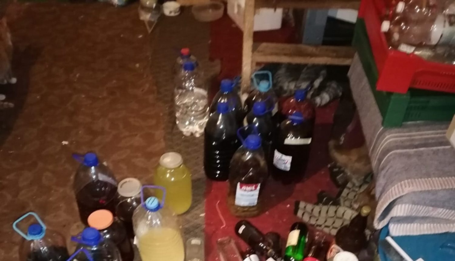Uz grīdas redzamas dažāda tilpuma pudeles ar dažādas krāsas nelikumīgu alkoholu