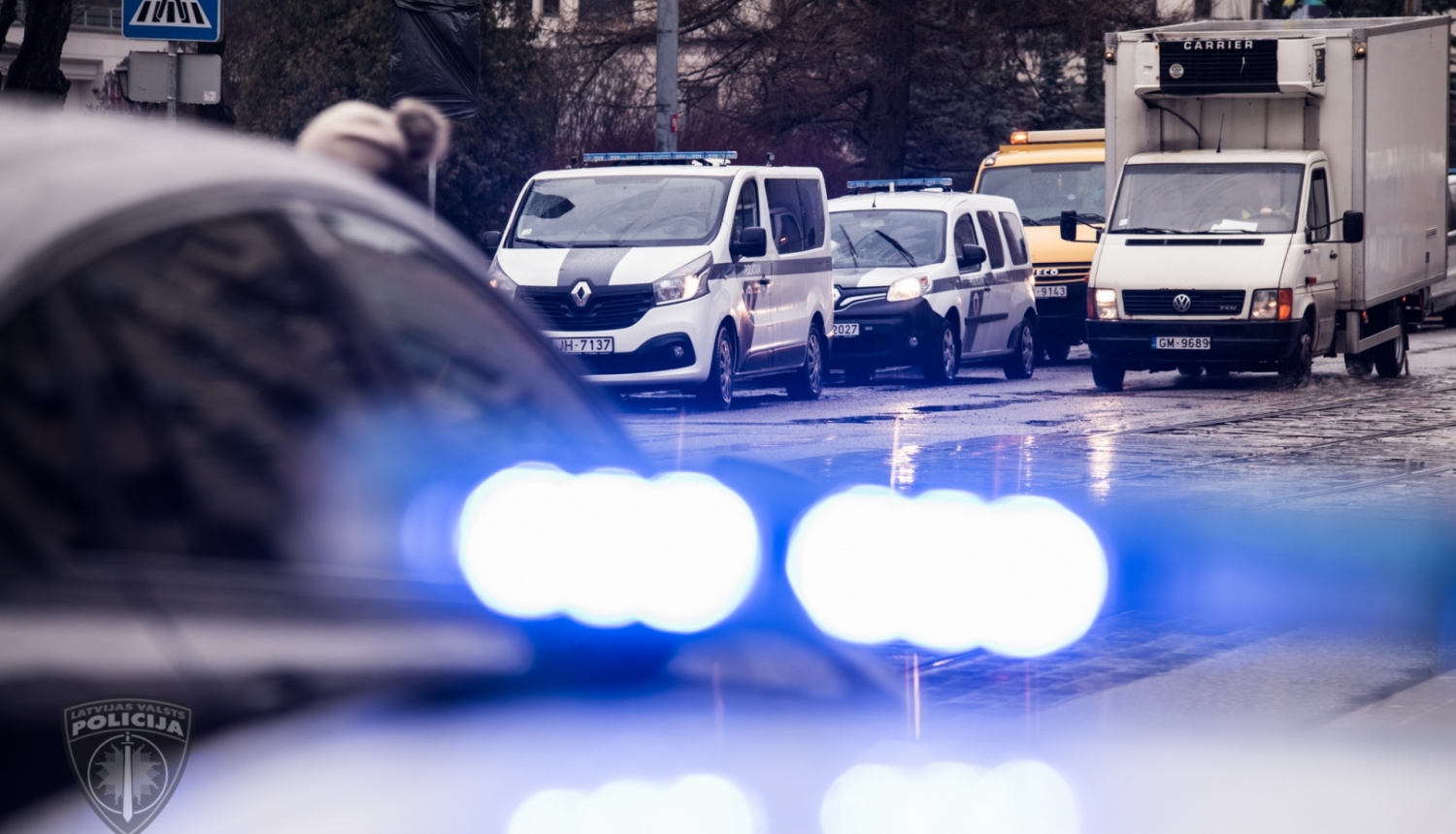 foto ar satiksmi un policijas auto ar ieslēgtām zilām bākugunīm
