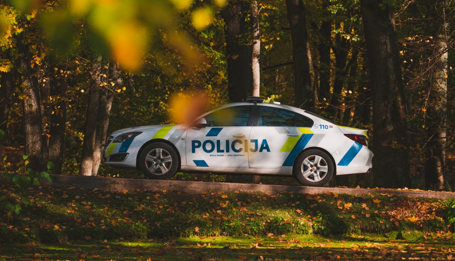 Policijas automašīna stāv uz ceļa, visapkārt koki, krāsainās rudens lapās