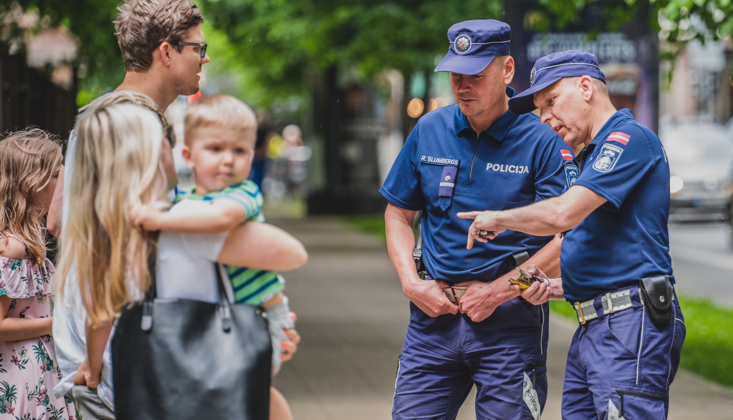 Divi policisti uz ielas komunicē ar pieaugušu vīrieti, sievieti un 2 bērniem
