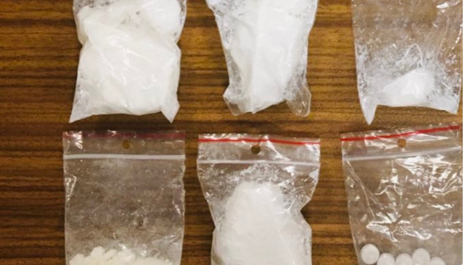 Seši caurspīdīgas plastmasas maisiņi, kuros ir baltas krāsas pulverveida viela un vienā vairākas baltas krāsas tabletes