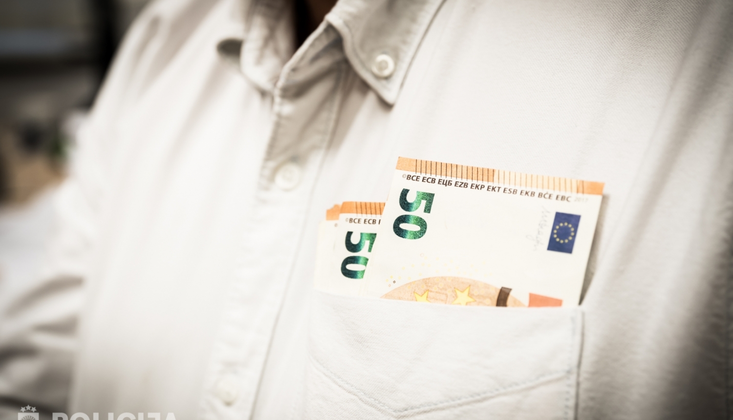 Ciilvēkam mugurā balts krekls un priekšējā krekla kabatā redzama daļa no 50 eiro banknotēm