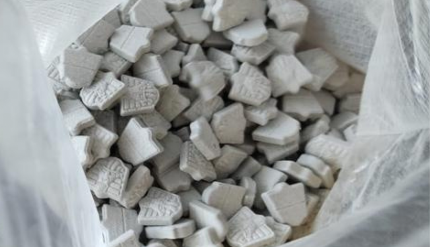 Atvērts polietilēna maiss un tajā redzamas daudz pelēkas MDMA tabletes 